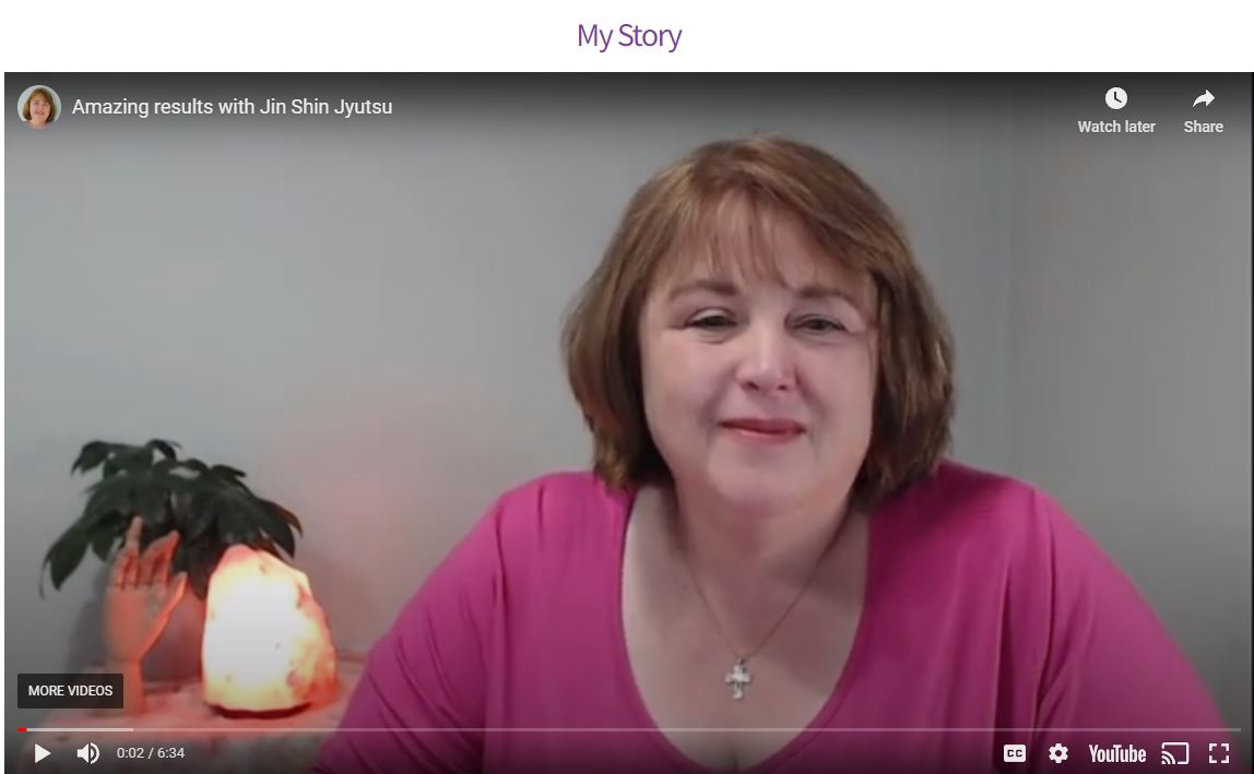 Jackie smiling - woman with medium brown hair in a fuscia top sitting on front of a salt lamp, wooden hand and plant.