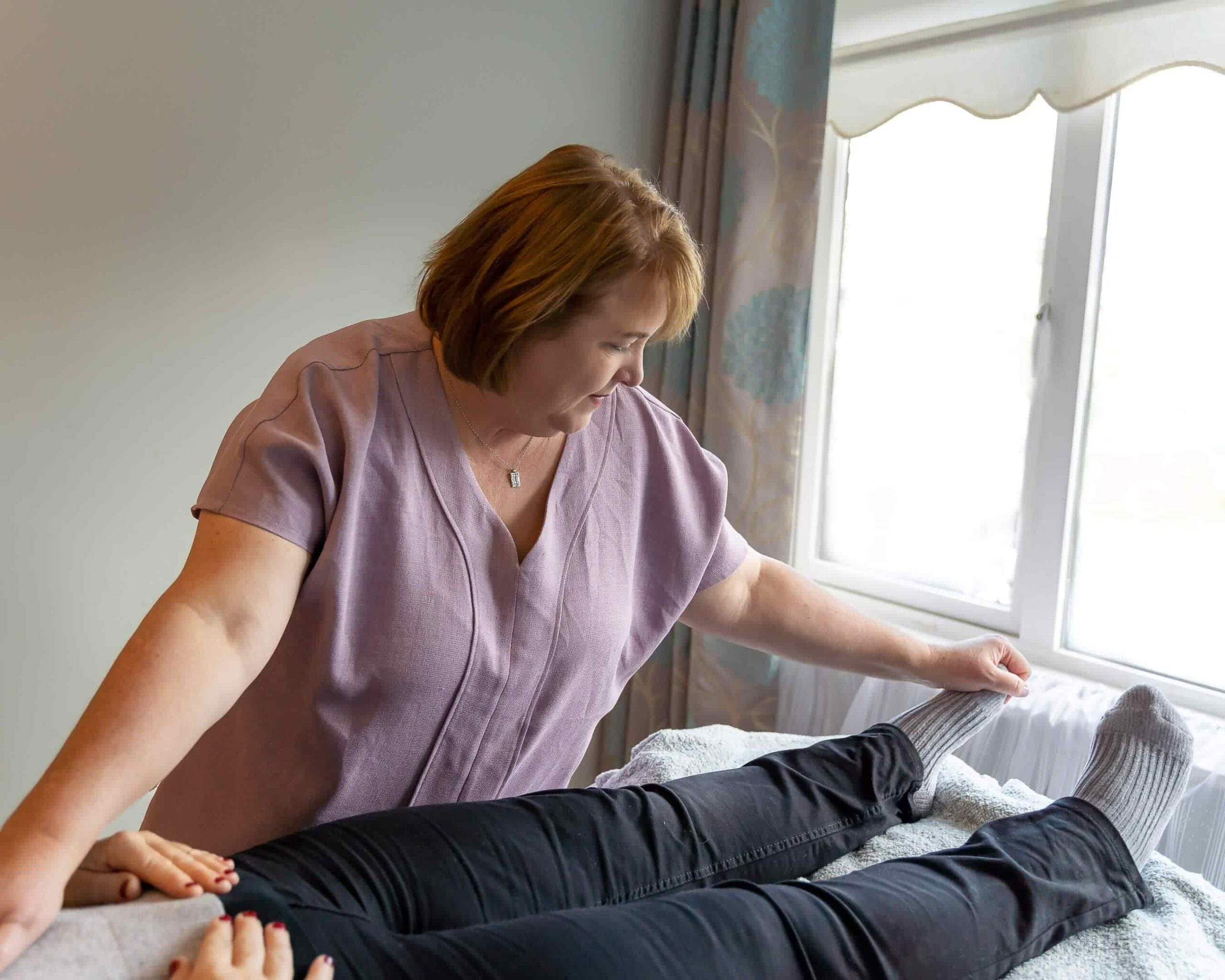 Jackie McGloughlin holistic therapist at Energy Flows giving a treatment to client who is resting on the padded plinth. Jackie is resting her hand on the client's tummy and holding the left foot - bringing harmony to their whole being.