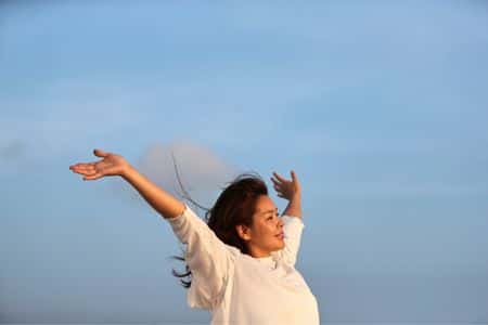 woman raising hands in open sky showing emotional freedom after Reiki